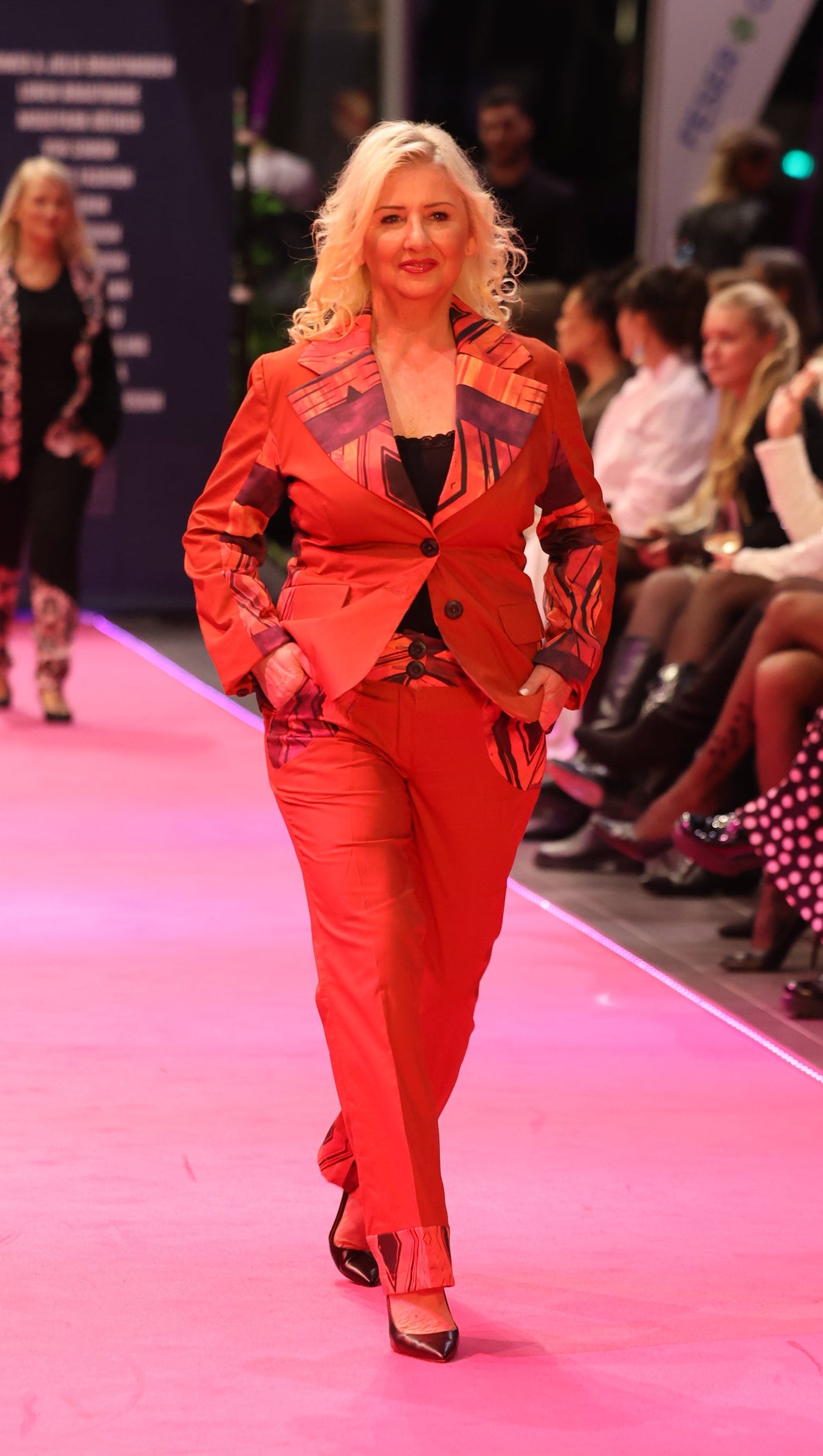 Model in a bright brown outfit walking on a pink runway.